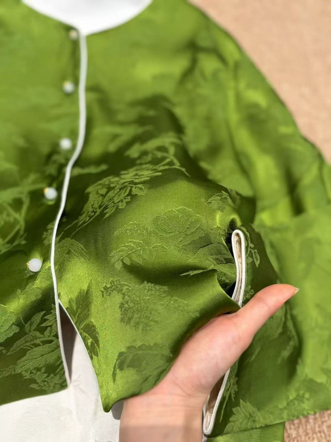 Close-up of jade green jacquard sleeve and ivory piping