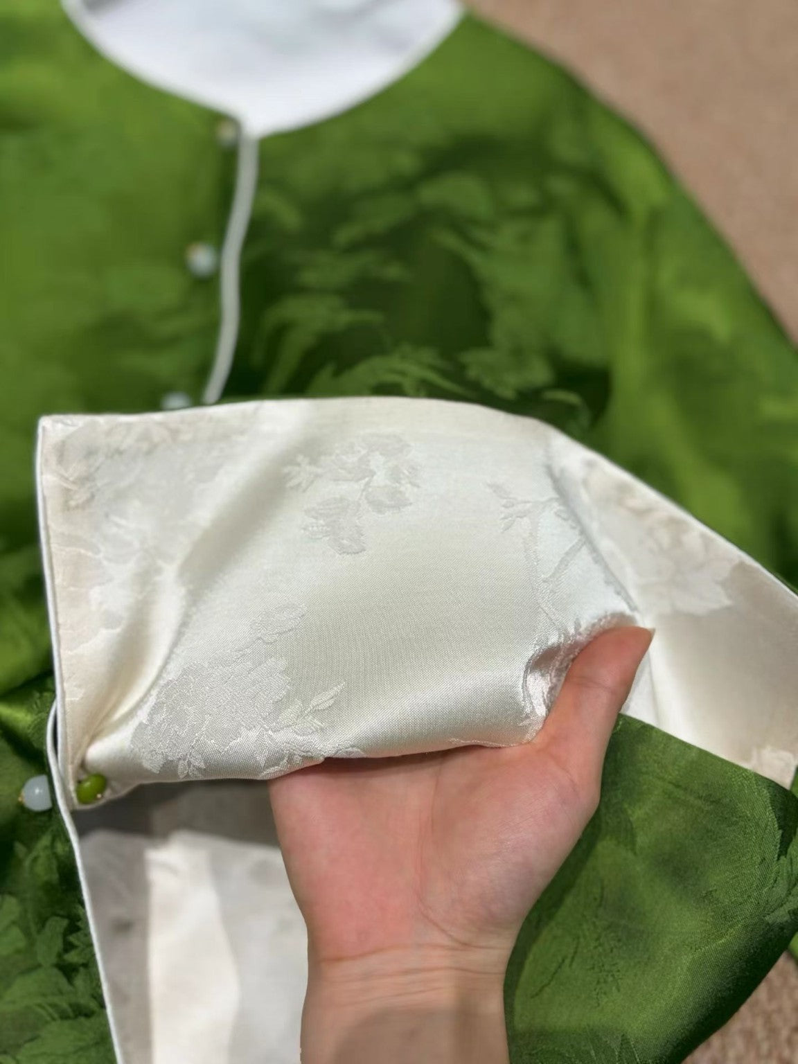 Close-up of ivory jacquard cuff against jade green jacket